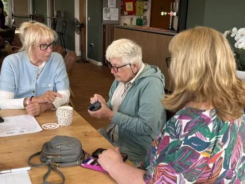 Two women helping an older woman with her phone at a table