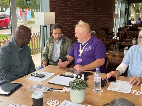 Dennis Hector and Pedro Lopez of Hailo-Ops at a table with a CDA Herts volunteer in a purple polo shirt, looking at a phone together