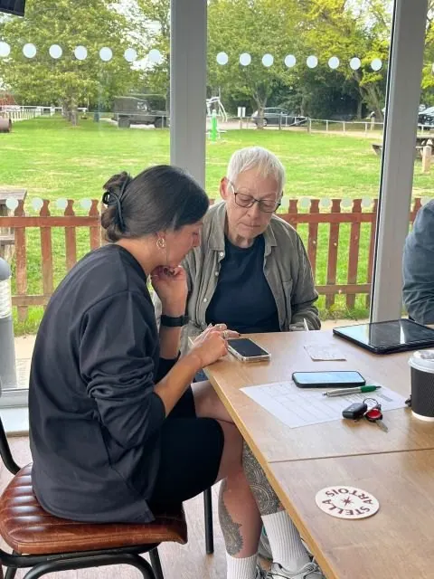 A volunteer working through a phone question with an older man beside a window